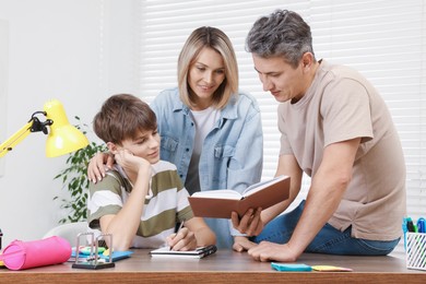 Parents helping their son with homework at table indoors