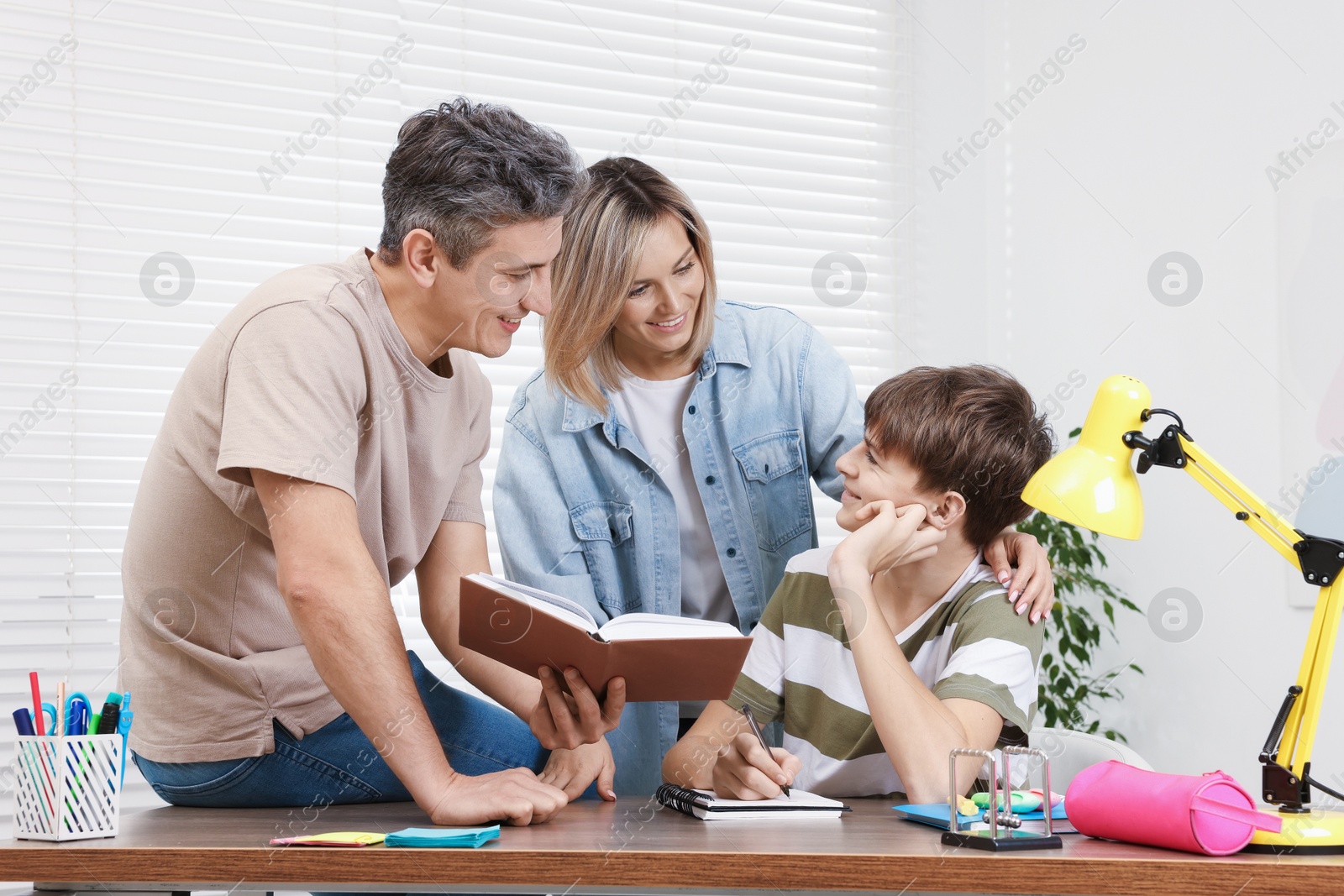 Photo of Smiling parents helping their son with homework at table indoors