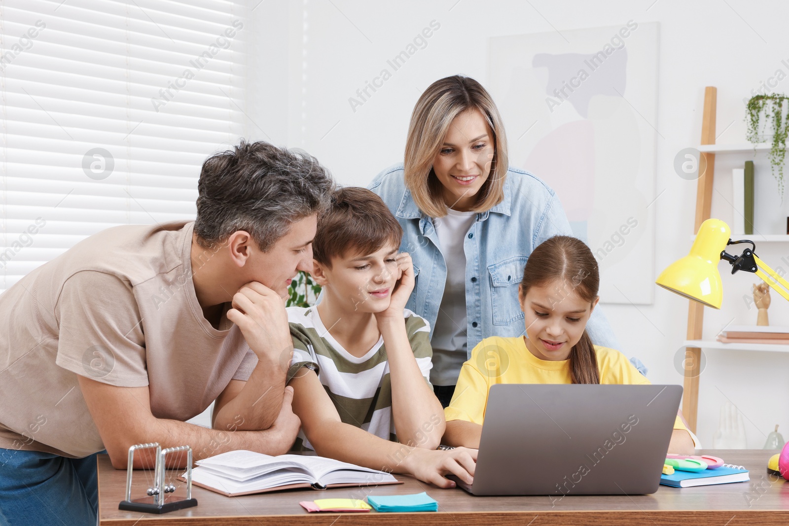 Photo of Parents and their children doing homework with laptop at table indoors