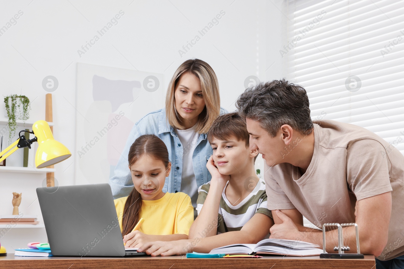 Photo of Parents and their children doing homework with laptop at table indoors