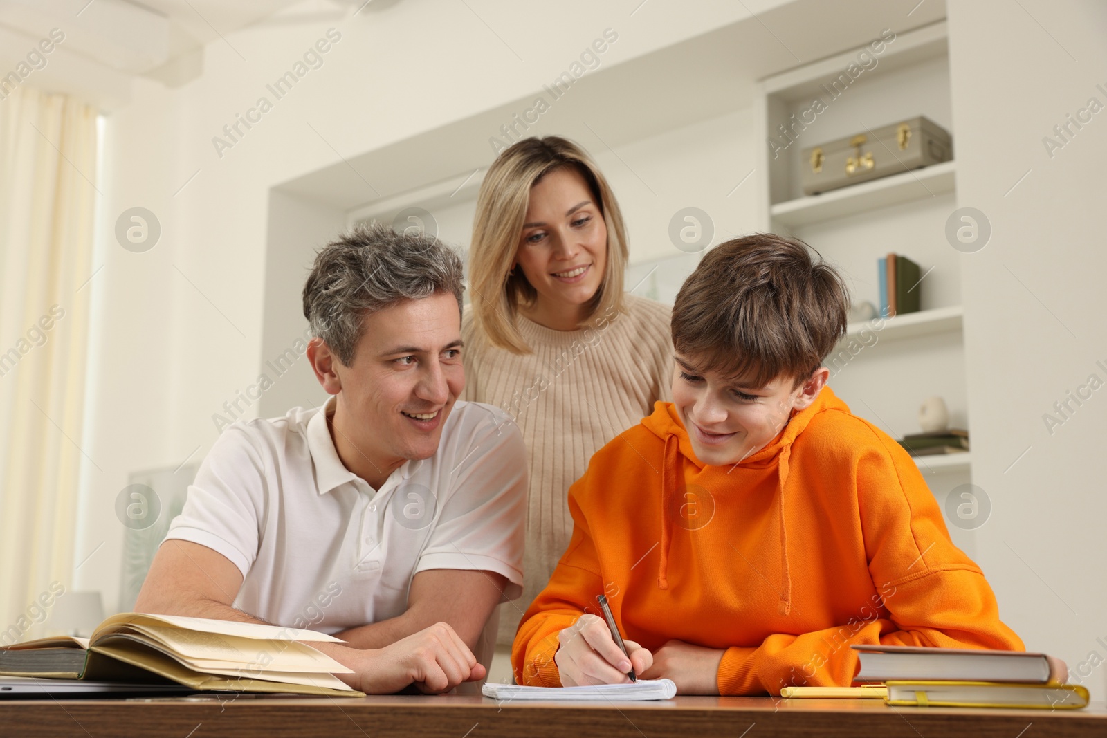 Photo of Parents helping their son with homework at table indoors, low angle view