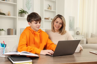 Smiling mother and her son doing homework with laptop at table indoors