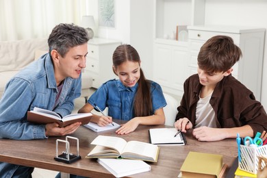 Photo of Father helping his children with homework at table indoors