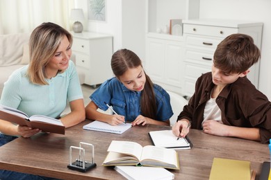 Photo of Smiling mother helping her children with homework at table indoors