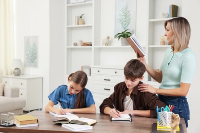 Photo of Mother helping her children with homework at table indoors. Space for text