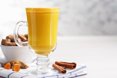 Photo of Delicious turmeric latte and rhizomes on white wooden table, closeup. Space for text