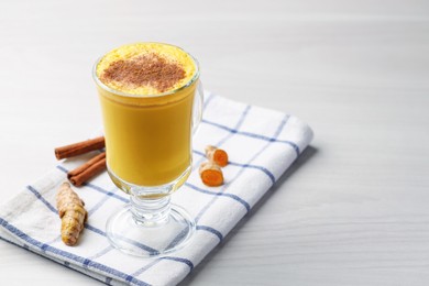 Delicious turmeric latte and rhizomes on white wooden table, closeup. Space for text