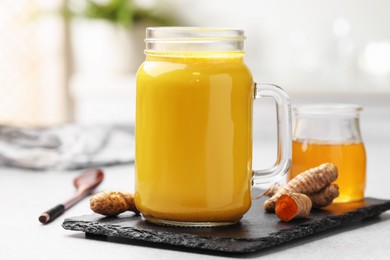 Delicious turmeric latte with honey and rhizomes on grey table, closeup