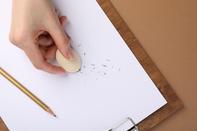 Photo of Woman rubbing eraser against paper at brown table, top view