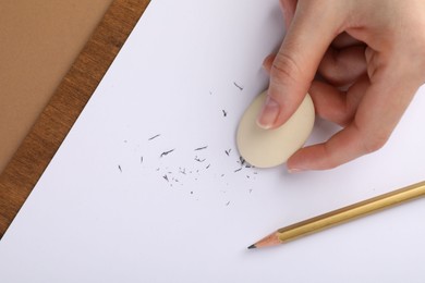 Photo of Woman rubbing eraser against paper at brown table, top view