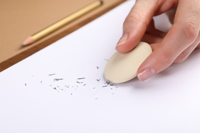 Photo of Woman rubbing eraser against paper at brown table, closeup