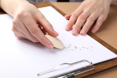 Photo of Woman rubbing eraser against paper at brown table, closeup