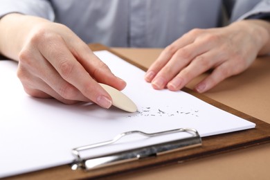 Photo of Woman rubbing eraser against paper at brown table, closeup