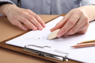 Photo of Woman rubbing eraser against paper at brown table, closeup