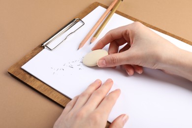 Photo of Woman rubbing eraser against paper at brown table, closeup