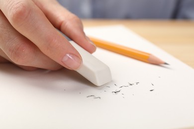 Photo of Woman rubbing eraser against paper at wooden table, closeup