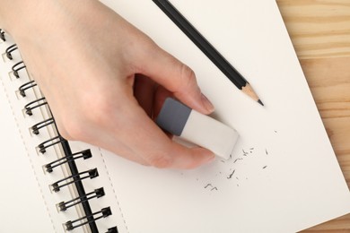 Photo of Woman rubbing eraser against paper at wooden table, top view