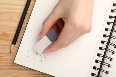 Photo of Woman rubbing eraser against paper at wooden table, top view