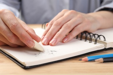 Photo of Woman rubbing eraser against paper at wooden table, closeup