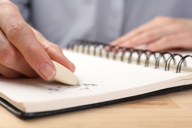 Photo of Woman rubbing eraser against paper at wooden table, closeup