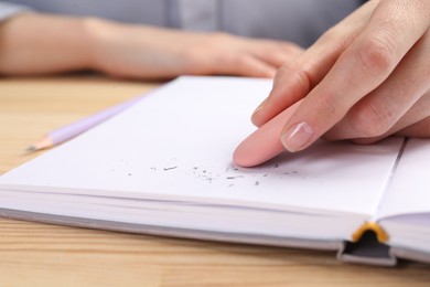 Photo of Woman rubbing eraser against paper at wooden table, closeup