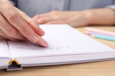 Photo of Woman rubbing eraser against paper at wooden table, closeup