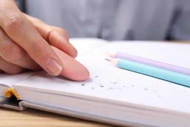 Photo of Woman rubbing eraser against paper at wooden table, closeup