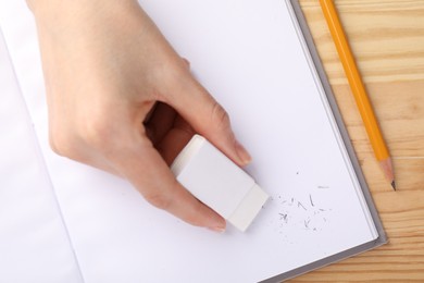 Photo of Woman rubbing eraser against paper at wooden table, top view