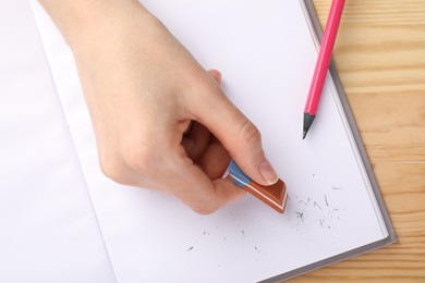 Photo of Woman rubbing eraser against paper at wooden table, top view