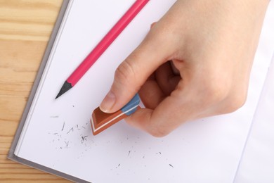 Photo of Woman rubbing eraser against paper at wooden table, top view