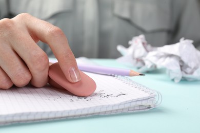 Photo of Woman rubbing eraser against paper at light blue table, closeup