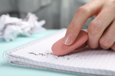 Photo of Woman rubbing eraser against paper at light blue table, closeup