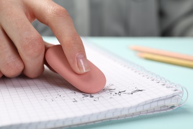 Photo of Woman rubbing eraser against paper at light blue table, closeup