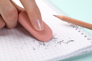 Photo of Woman rubbing eraser against paper at light blue table, closeup