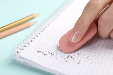 Photo of Woman rubbing eraser against paper at light blue table, closeup