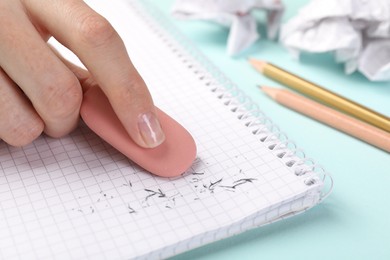 Photo of Woman rubbing eraser against paper at light blue table, closeup