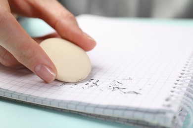 Photo of Woman rubbing eraser against paper at light blue table, closeup