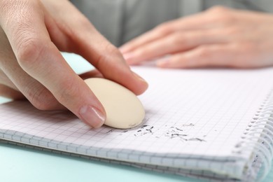 Photo of Woman rubbing eraser against paper at light blue table, closeup