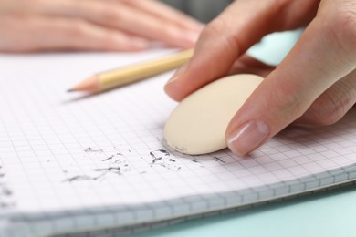 Photo of Woman rubbing eraser against paper at light blue table, closeup