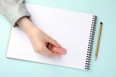 Photo of Woman rubbing eraser against paper at light blue table, top view