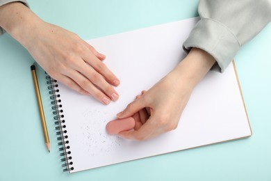 Photo of Woman rubbing eraser against paper at light blue table, top view