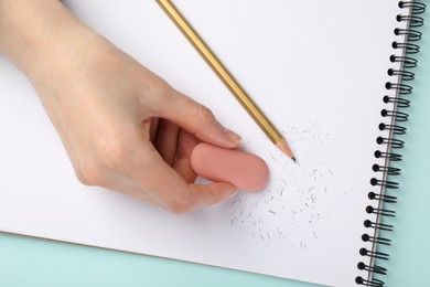 Photo of Woman rubbing eraser against paper at light blue table, top view