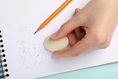 Photo of Woman rubbing eraser against paper at light blue table, closeup