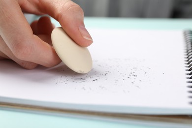 Photo of Woman rubbing eraser against paper at light blue table, closeup