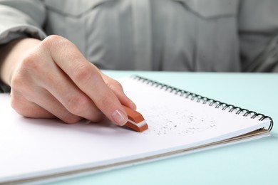 Photo of Woman rubbing eraser against paper at light blue table, closeup