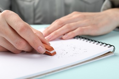 Photo of Woman rubbing eraser against paper at light blue table, closeup