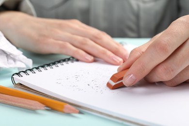 Photo of Woman rubbing eraser against paper at light blue table, closeup