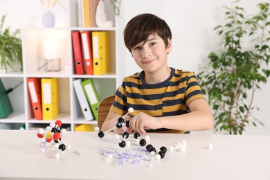 Photo of Boy making DNA structure model at desk indoors. Space for text