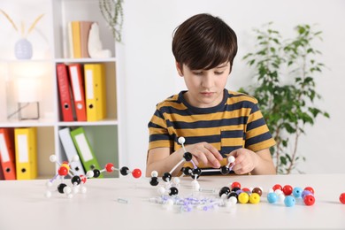 Photo of Boy making DNA structure model at desk indoors. Space for text