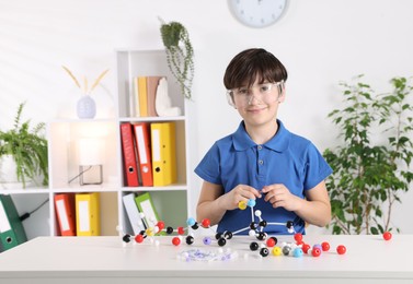 Boy making DNA structure model at desk indoors. Space for text